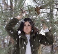 a woman is holding up a pine tree in the snow