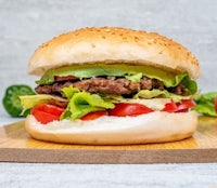 a burger with lettuce, tomatoes and avocado on a wooden cutting board