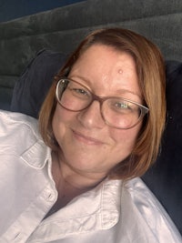a woman wearing glasses and a white shirt laying on a bed