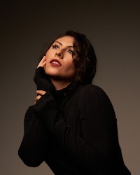 a woman in a black turtleneck shirt posing with her hand on her chin