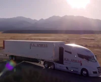 a semi truck driving down a road with mountains in the background