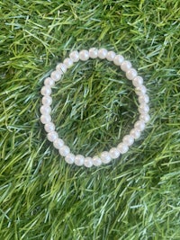 a white pearl bracelet laying on top of grass