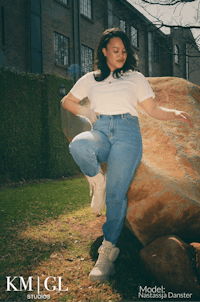 a woman in jeans and a white t - shirt sitting on a rock