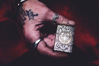 a hand holding a silver lighter with tattoos on it