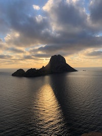 the sun is shining over a small island in the water