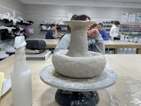 a woman is making a vase in a pottery studio