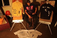 a man sitting on a stool next to several t - shirts