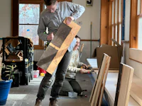a man and woman working on a piece of wood in a room