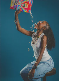 a woman is sitting on a stool with a box of cereal in her hands