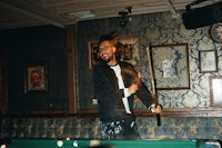 a man with dreadlocks standing next to a pool table