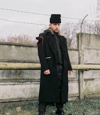 a man in a black coat standing next to a fence