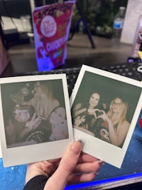 two people holding polaroid photos in front of a computer