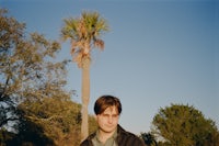 a man in a jacket standing next to a palm tree