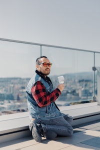 a man sitting on top of a building with a cup of coffee