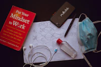 a notebook, earphones, and a phone on a table next to a coronavirus mask