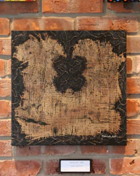 a black and brown painting hanging on a brick wall