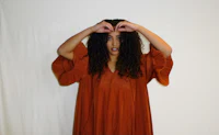 a woman in a brown dress making a heart with her hands