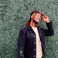 a man with dreadlocks leaning against a green wall