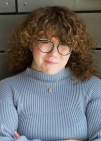 a woman with curly hair wearing glasses and a sweater