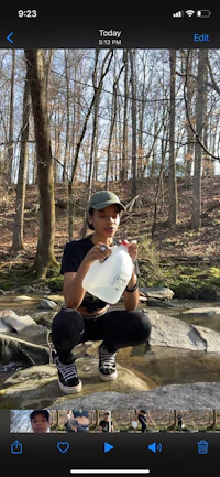 a woman is squatting down next to a stream in the woods