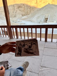 a man holding a photo on a balcony overlooking a desert