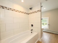 a white tiled bathroom with a tub and toilet