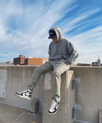 a man sitting on a concrete wall wearing a hoodie and sneakers