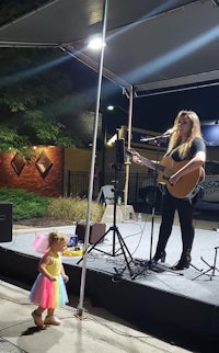 a young girl playing an acoustic guitar in front of a crowd