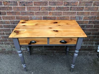 a small table with two drawers in front of a brick wall