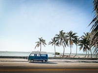 a blue camper van parked on the side of the road with palm trees in the background