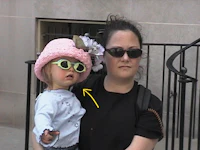 a woman holding a little girl wearing sunglasses and a pink hat