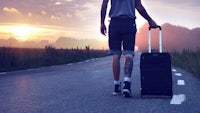 a man is walking down a road with a suitcase
