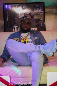 a man sitting on a couch wearing a hat and sunglasses