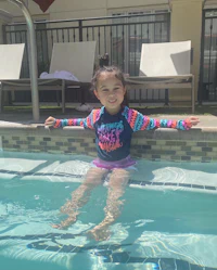 a young girl in a swimsuit sitting in a pool