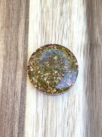 a green and brown glass button on top of a wooden table