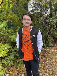 a girl wearing an orange and black t - shirt in the woods