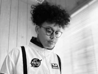 a black and white photo of a young man with glasses and suspenders