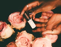 a hand holding a bottle of essential oil next to roses