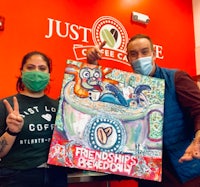 two people posing with a painting in front of a coffee shop