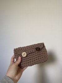 a person holding up a brown crocheted phone case