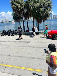 a group of people standing on the side of the road with a red car in the background