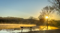 a misty sunrise over a lake with a bench
