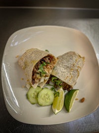 a burrito on a plate with cucumbers and limes