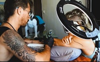 a man is getting tattooed by a woman in front of a mirror
