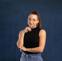 a young woman wearing glasses and jeans posing on a blue background