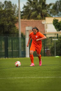 a woman in an orange uniform kicking a soccer ball