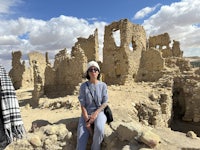 a woman sits in front of ruins in the desert