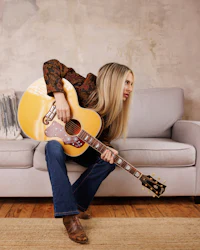 a woman playing an acoustic guitar on a couch