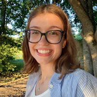 a young woman in glasses smiles in front of a tree
